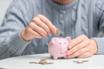 Man putting coin into piggy bank at white table, closeup