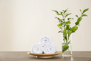 Fresh rolled towels and green branches on grey wooden table