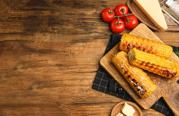 Delicious grilled corn cobs on wooden table, flat lay. Space for text