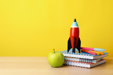 Bright toy rocket and school supplies on wooden table. Space for text