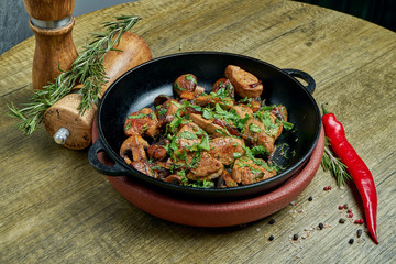 Fried potatoes with pork, onions and herbs in a decorative pan on a wooden background. Top view on tasty food.