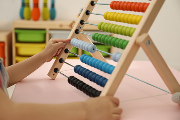 Cute child playing with wooden abacus at table in room, closeup