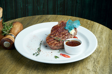 Juicy and mouth-watering grilled ribeye steak with spicy butter on a black tray with a side dish of vegetables. American cuisine.. Close up. Wooden background