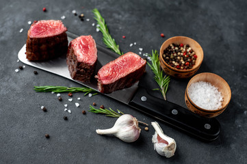 Three slices of grilled steak over meat knife with spices on a stone background with copy space for your text