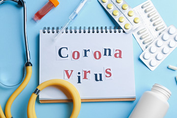 Flat lay composition of medications and notebook with words CORONA VIRUS on light blue background