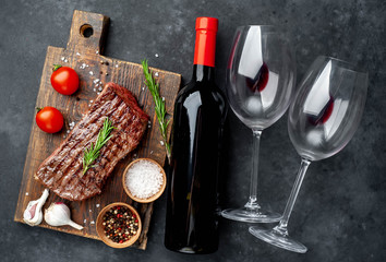 grilled beef steak on a wooden board and a bottle of wine and glasses on a stone background