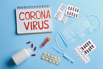 Flat lay composition of medications and notebook with words CORONA VIRUS on light blue background