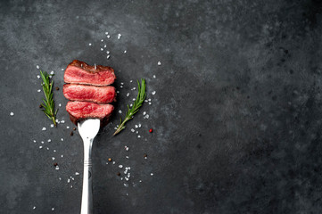 grilled slices of beef meat on a meat fork with spices on a stone background with copy space for...