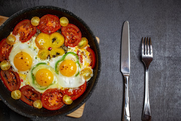 Fried eggs in a frying pan with cherry tomatoes and bell pepper for breakfast on a black background.