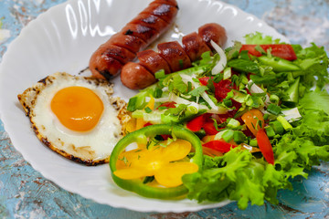 Fried eggs in a plate with sausages, cherry tomatoes and bell pepper for breakfast,