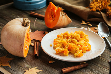  Millet porridge with pumpkin on a white plate, pumpkin slices, autumn leaves and cinnamon sticks on an old wooden table.