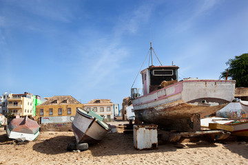 Fototapeta premium Old weathered boats parked on the beach of Sal Rei with colorful houses in the background on Boa Vista in Cape Verde