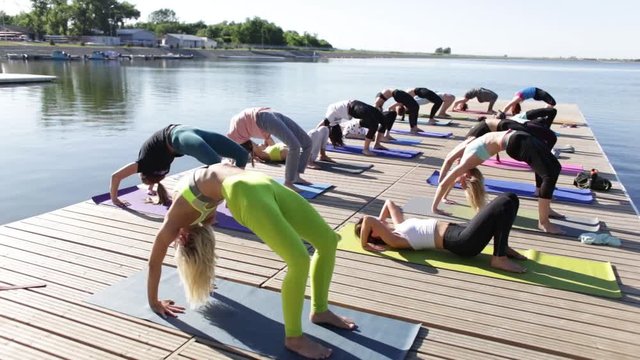 in the morning a group of people do yoga on the pier by the lake, summer time