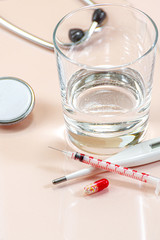 Red pills, thermometer, syringe and a glass of water on a beige pastel background.