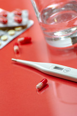 Antibiotics, a glass of water and a thermometer on a red background. Photo shallow depth of field..