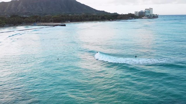 A surfer catches a wave as the sun rises in Oahu with DiamondHead towering over. Talk about a beautiful place to surf.