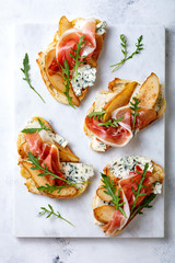 Appetizer crostini, tapas, open faced sandwiches with pear, prosciutto, arugula and blue cheese on white marble board. Delicious snack, appetizers