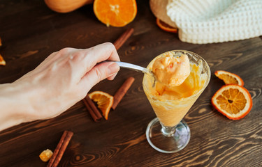  Melted pumpkin ice cream in a spoon on a wooden background. Spoon with orange ice cream in a female hand.
