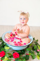 Little cute baby girl is sitting in a basin with pink petals and strawberries.