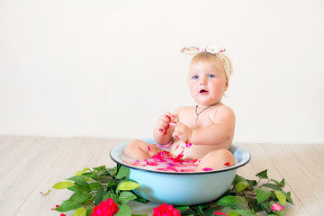 Little cute baby girl is sitting in a basin with pink petals and strawberries.