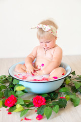 Little cute baby girl is sitting in a basin with pink petals and strawberries.