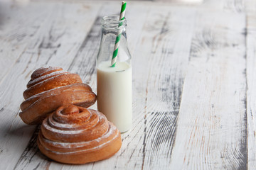 fresh homemade cinnamon rolls on a wooden cutting desk and milk in glass bottle