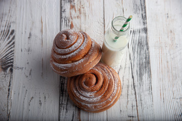 fresh homemade cinnamon rolls on a wooden cutting desk and milk in glass bottle