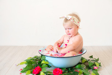 Little cute baby girl is sitting in a basin with pink petals and strawberries.