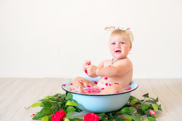 Little cute baby girl is sitting in a basin with pink petals and strawberries.