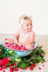 Little cute baby girl is sitting in a basin with pink petals and strawberries.