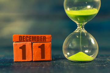 december 11th. Day 11 of month,Handmade wood cube with date month and day and hourglass with green sand. Time passing away. artistic coloring.  winter month, day of the year concept