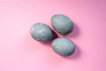 Gray colored easter eggs on pink background. Three eggs dyed in color of concrete. Top view, flat lay. Happy Easter concept