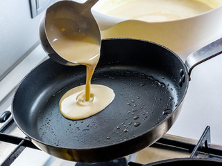 Batter pouring out of a metal bucket onto a red-hot greased frying pan. The process of baking pancakes.