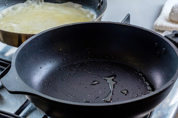 Drops of hot oil in a hot pan. In the background is a frying pan in which a rosy pancake is baked. Home kitchen.