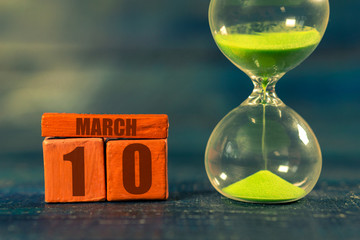 march 10th. Day 10 of month,Handmade wood cube with date month and day and hourglass with green sand. Time passing away. artistic coloring.  spring month, day of the year concept