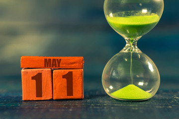 may 11th. Day 11 of month,Handmade wood cube with date month and day and hourglass with green sand. Time passing away. artistic coloring.  spring month, day of the year concept