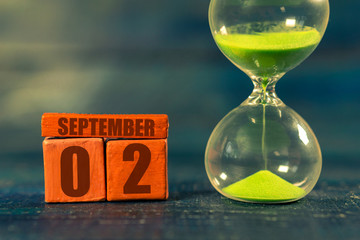 september 2nd. Day 2 of month,Handmade wood cube with date month and day and hourglass with green sand. Time passing away. artistic coloring.  autumn month, day of the year concept