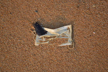 An old medical mask fell into the sand on a beach