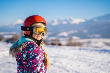 Little girl wearing white helmet and outwear holding mountain skis in sunlight