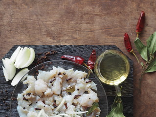 XE salad of freshly salted river pike fish on a cutting kitchen board with ingredients for cooking. Pike fillet pieces. Wooden brown background.