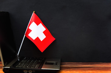  flag of Switzerland , computer, laptop on table and dark background