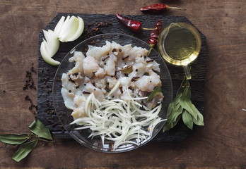 XE salad of freshly salted river pike fish on a cutting kitchen board with ingredients for cooking. Pike fillet pieces. Wooden brown background.