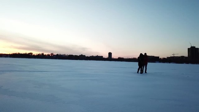 Couple/ friends playing/ walking on a frozen lake during blue hour filmed with a drone, spinning