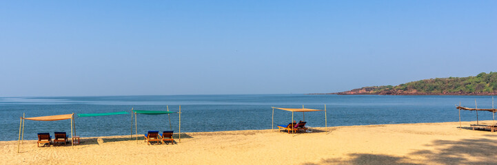 Sand beach with sun loungers background.  Deckchairs. Panorama of  the coast of Goa, India.  Beautiful view of tropical ocean beach with long blue waves rolling. Banner. Header.
