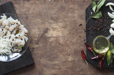 XE salad of freshly salted river pike fish on a cutting kitchen board with ingredients for cooking. Pike fillet pieces. Wooden brown background.