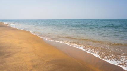 Panorama of long surf waves on the coast.   Sand beach background. Beautiful view of tropical ocean beach with long blue waves rolling. 