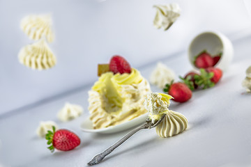 Pavlov’s (pavlova) cake with strawberries, on a white saucer, vintage spoon, strawberries falling from a white cup, next to meringues, meringues fly, white background, high key