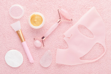 golden facial cream mask with a brush, jade roller and silicone beauty mask on pink background © nadisja
