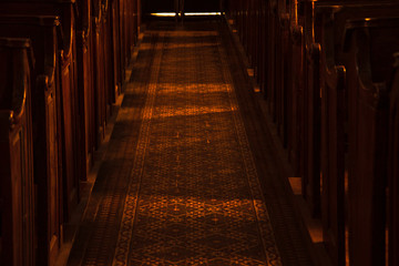 Temple mystery. Wooden benches in dark empty church. Sunlight lightens the pews and passage floor with beautiful pattern. Religious background. Divine light, grace, hope, miracle concepts.