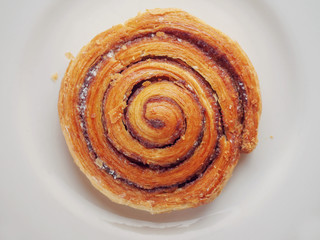 One crispy cinnamon roll on a white plate.Top view, close up.